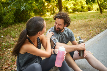 Friends relax in a lush green park after a workout, chatting happily while sipping drinks and...