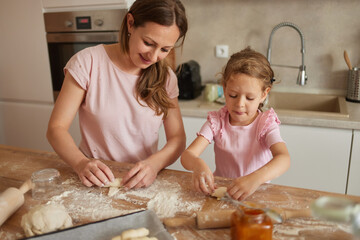 In a cheerful kitchen, a mother and her young daughter bond as they roll and shape dough, sharing...