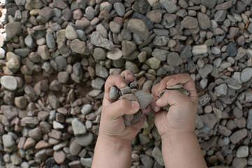 Two small hands full of stones during outdoor play on forest floor. Child’s hands holding small stones with blurred rocky floor background. 
