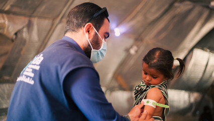 A doctor examines children's malnutrition inside a refugee camp. Malnutrition was measured using a mid-upper arm circumference belt.
