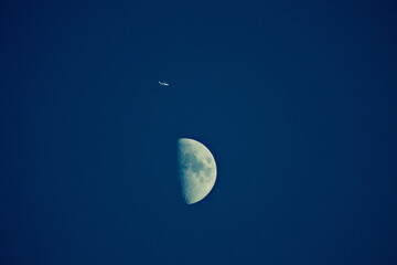 Passenger airplane visually flying over half moon, strong telephoto effect with lunar background...