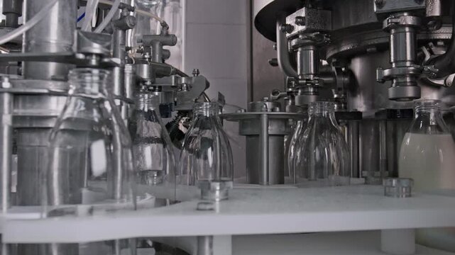 Automated machinery fills glass bottles with milk on a production line within a dairy or bottling plant, emphasizing industrial food processing and packaging
