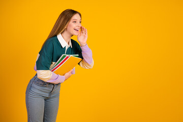 Cheerful young woman holding colorful notebooks, gesturing joyfully against bright yellow background