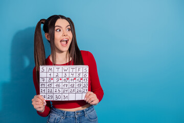 Young woman holding calendar with hearts on marked dates against blue background, expressing...