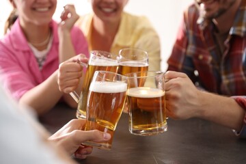 Friends clinking glasses of beer at grey table indoors, closeup