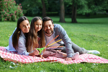 Happy family blowing soap bubbles on checkered picnic blanket in park