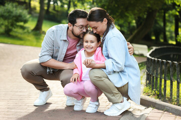 Family weekend. Parents kissing their happy daughter in park