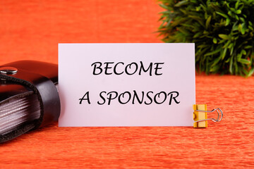 BECOME A SPONSOR text written on a white card near the business card holder in black on an orange...