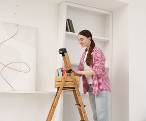 Woman putting books on shelves using ladder at home