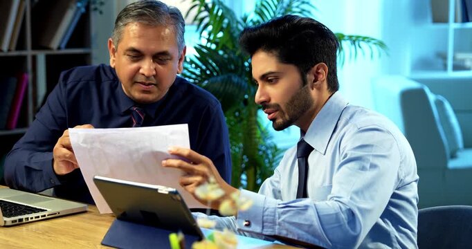 Businessmen with laptop and documents working together in modern office at desk, Indian Asian corporate professionals in formal attire focused on teamwork, planning, strategy, collaboration concept