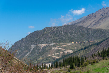 Ala-Archa Park, Mountain base camp nestled on steep hillside, zigzag trail ascending, dense pine...