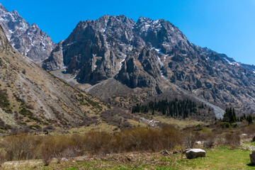 Ala-Archa Park, Towering mountain range with steep cliffs, rocky slopes, patches of snow, grassy...