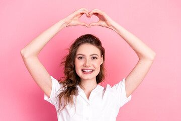 Young woman with hands forming a heart shape, vibrant pink background, wearing casual white shirt,...