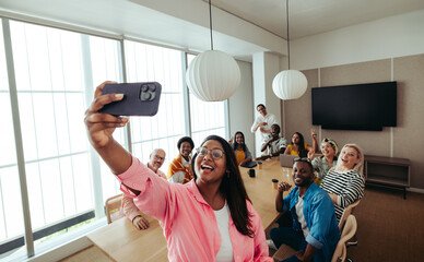 Marketing team taking a group selfie around a conference table during a meeting in a modern office...