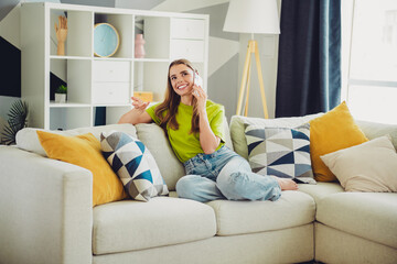 Young woman relaxing on a cozy sofa in a modern living room with colorful cushions, embracing...