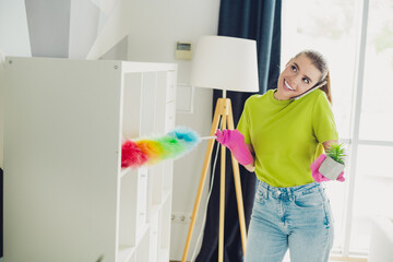 Young woman multitasking cleaning and chatting happily in a cozy living room interior with modern...