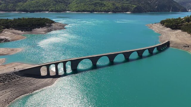 Aerial summer view of Serre-Poncon Lake with Chanteloube Bay and old viaduct. Sunlight reflecting on the water surface in the Durance Valley. French Alps, Hautes-Alpes, France