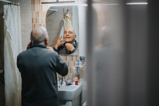 Senior man maintaining personal grooming by shaving in front of a bathroom mirror, expressing confidence and positivity. The cozy bathroom setting adds warmth and familiarity to the scene.