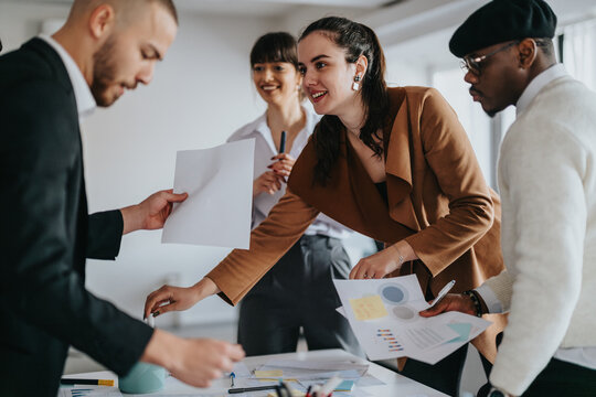 Group of business professionals working together on a project in a modern office environment. They discuss ideas while reviewing documents and charts during a casual and collaborative team meeting.