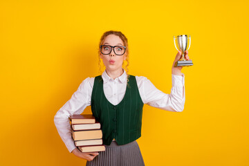 Cheerful student holding a trophy and books on a yellow background celebrating academic achievement
