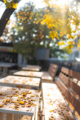 Table and bench in street cafe covered with fallen autumn leaves, autumn city background