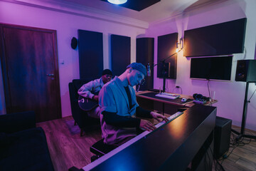 Two multiracial musicians collaborate in a recording studio, playing piano and guitar. The ambiance...