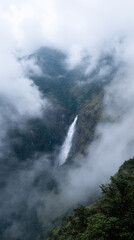 Misty mountain landscape with distant waterfall cascading through lush greenery