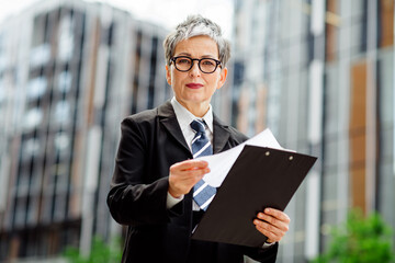 Professional woman outdoors holding documents in urban setting, representing determination in...