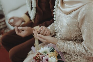 Close-up of bride and groom praying during traditional Indonesian Muslim wedding ceremony, wearing...