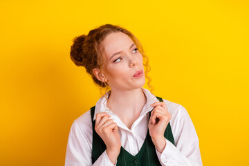 Young woman with red hair in white shirt and green waistcoat on yellow background looking...