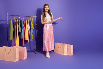 Fashionable young woman presenting colorful outfits with shopping bags on a stylish purple...