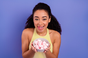 Charming young woman in a yellow dress enjoying sweet treats in a white bowl against a purple...