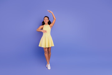 Young fashionable woman in a yellow dress posing joyfully against a vibrant purple background...