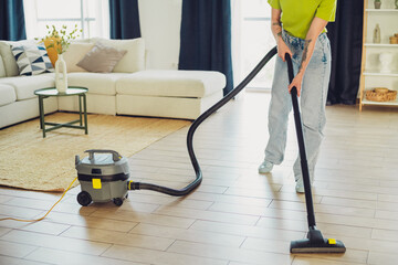 Woman in casual attire vacuuming a modern living room with a stylish interior design on a bright...
