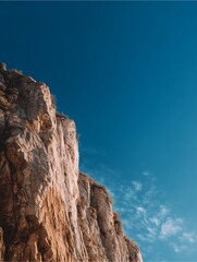 Fototapeta premium Majestic Rock Face and Sky: A weathered rock face rises majestically against a vibrant blue sky, with subtle wisps of clouds adding texture to the canvas of the heavens, showcasing natural beauty