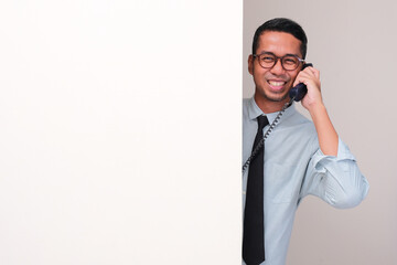 An employee peeking behind a wall smiling happy while on phone call