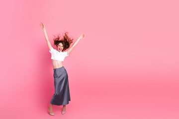 Energetic young woman in stylish attire dancing joyfully against a vibrant pink background