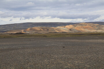 Volcanic landscape in the Icelandic highlands with black sand, colorful mountains and an overcast sky with ominous clouds