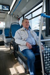 A portrait of an elderly man in casual clothes, sitting on a public bus and looking out the window.
