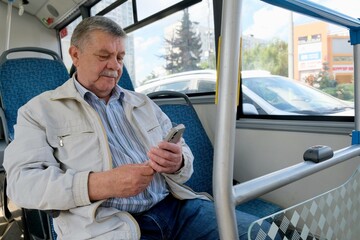 An elderly man uses a smartphone on public transportation. A pensioner on a bus
