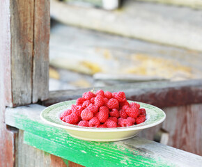 Fresh raspberry in a beautiful ceramic green plate on the old veranda railing in the garden. Selective focus.