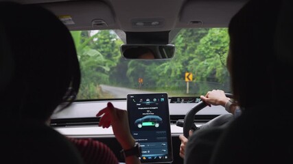 Happy beautiful asian woman friends driver electric car along a scenic winding road, surrounded by lush greenery. The digital touchscreen displays the car's battery level and charging options. - Powered by Adobe