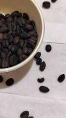 A bowl of freshly roasted coffee beans is dark in color, on a white background.