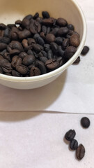 A bowl of freshly roasted coffee beans is dark in color, on a white background.