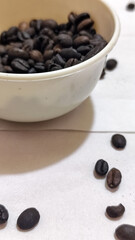 A bowl of freshly roasted coffee beans is dark in color, on a white background.