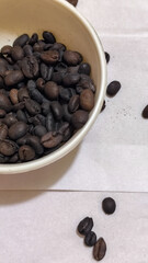 A bowl of freshly roasted coffee beans is dark in color, on a white background.