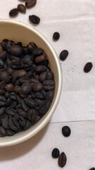 A bowl of freshly roasted coffee beans is dark in color, on a white background.