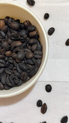 A bowl of freshly roasted coffee beans is dark in color, on a white background.