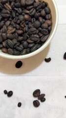 A bowl of freshly roasted coffee beans is dark in color, on a white background.