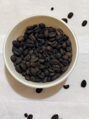 A bowl of freshly roasted coffee beans is dark in color, on a white background.